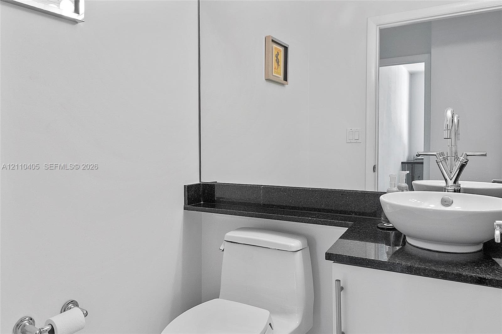Vanity with a white vessel sink, dark stone countertop, white cabinetry, chrome faucet, and wall-to-wall mirror