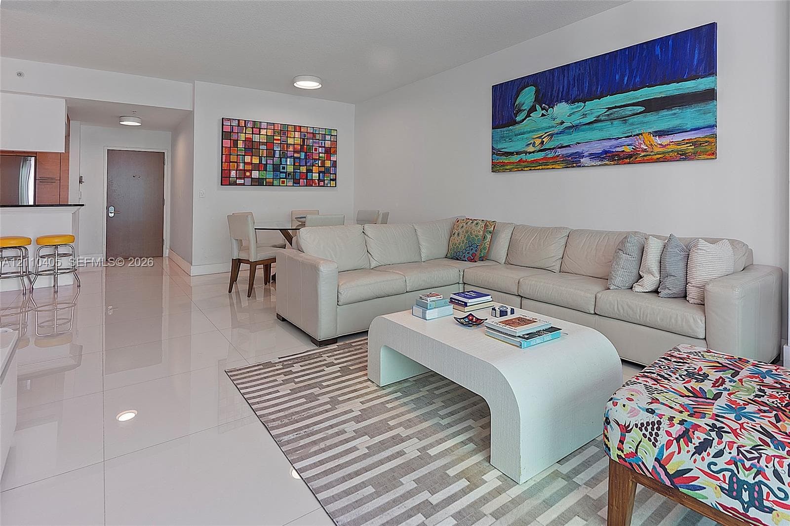 Open-concept interior featuring large-format porcelain tile flooring, recessed ceiling lighting, and a breakfast bar with stone-surface countertop