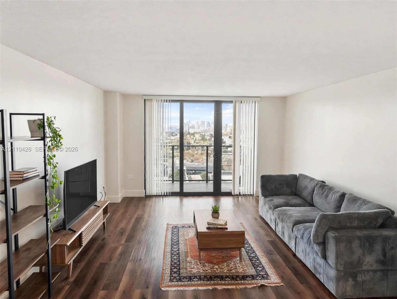 Living area featuring wood-finish flooring, floor-to-ceiling glass door, and balcony access with city skyline backdrop