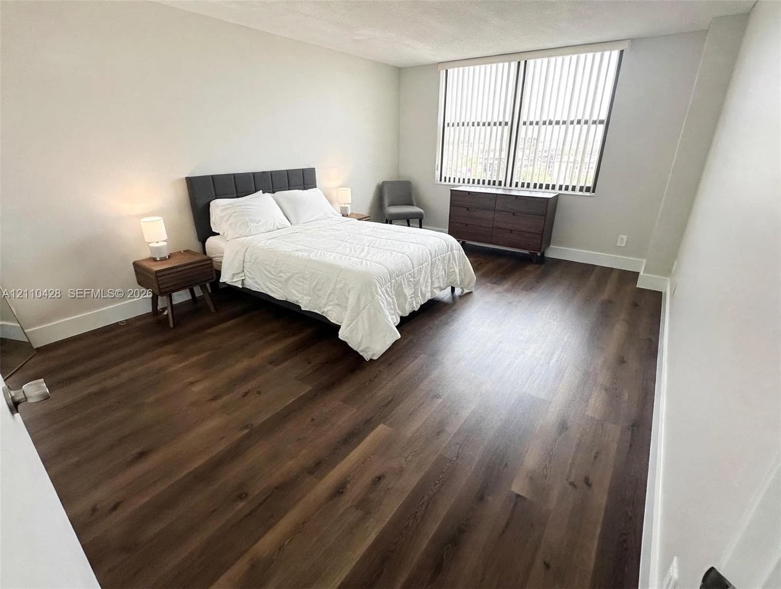 Neutral-toned interior space featuring wood-finish flooring and a large window with vertical blinds