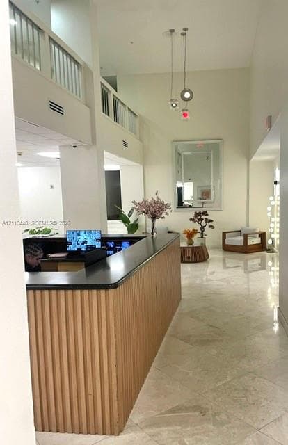High-ceilinged foyer featuring a built-in reception desk with a ribbed wood-finish base and dark stone countertop, polished tile flooring, and a multi-pendant light fixture