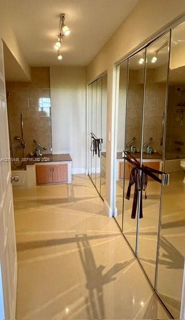 Light-toned tile flooring, built-in cabinetry with stone-finish countertops, full-length mirrored closet doors, and adjustable track lighting