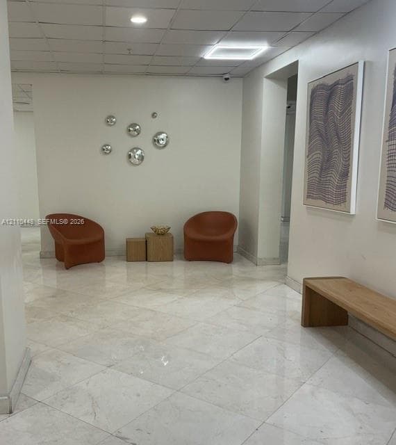 Polished stone flooring in a diagonal tile pattern, drop ceiling with integrated recessed lighting, and wall-mounted security fixtures