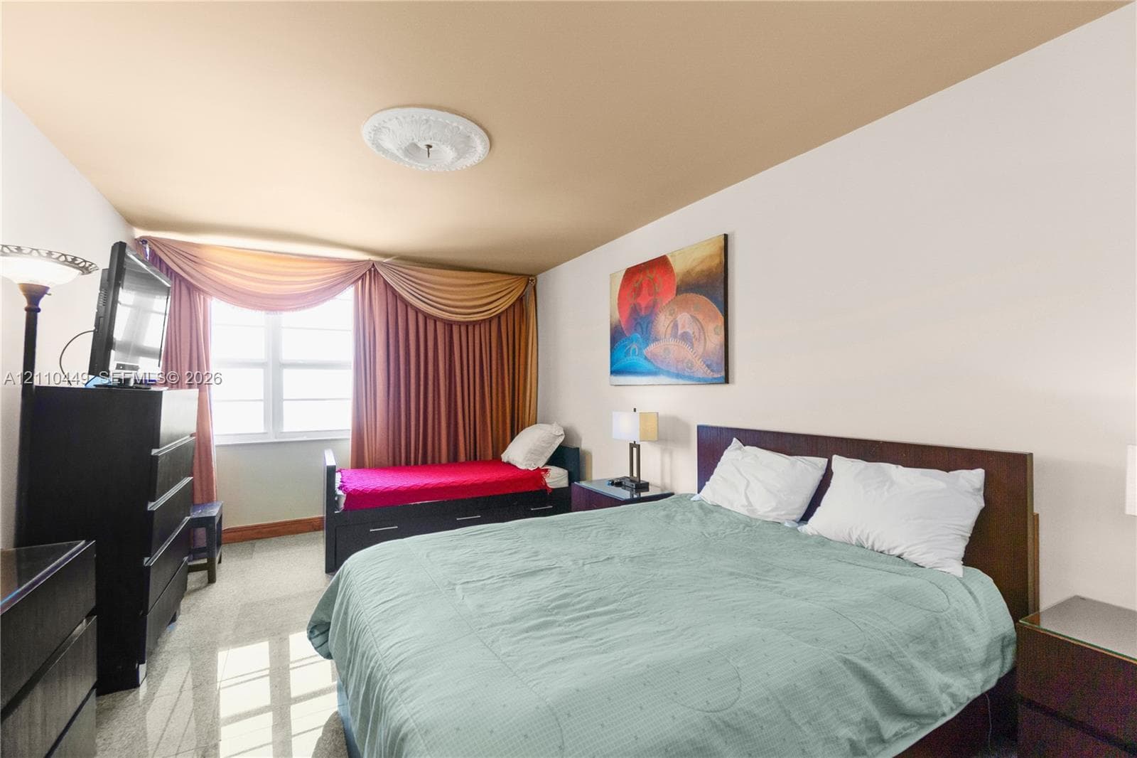 Neutral-toned room featuring a white ceiling with decorative plaster medallion, natural light from a large window, and polished stone-finish flooring
