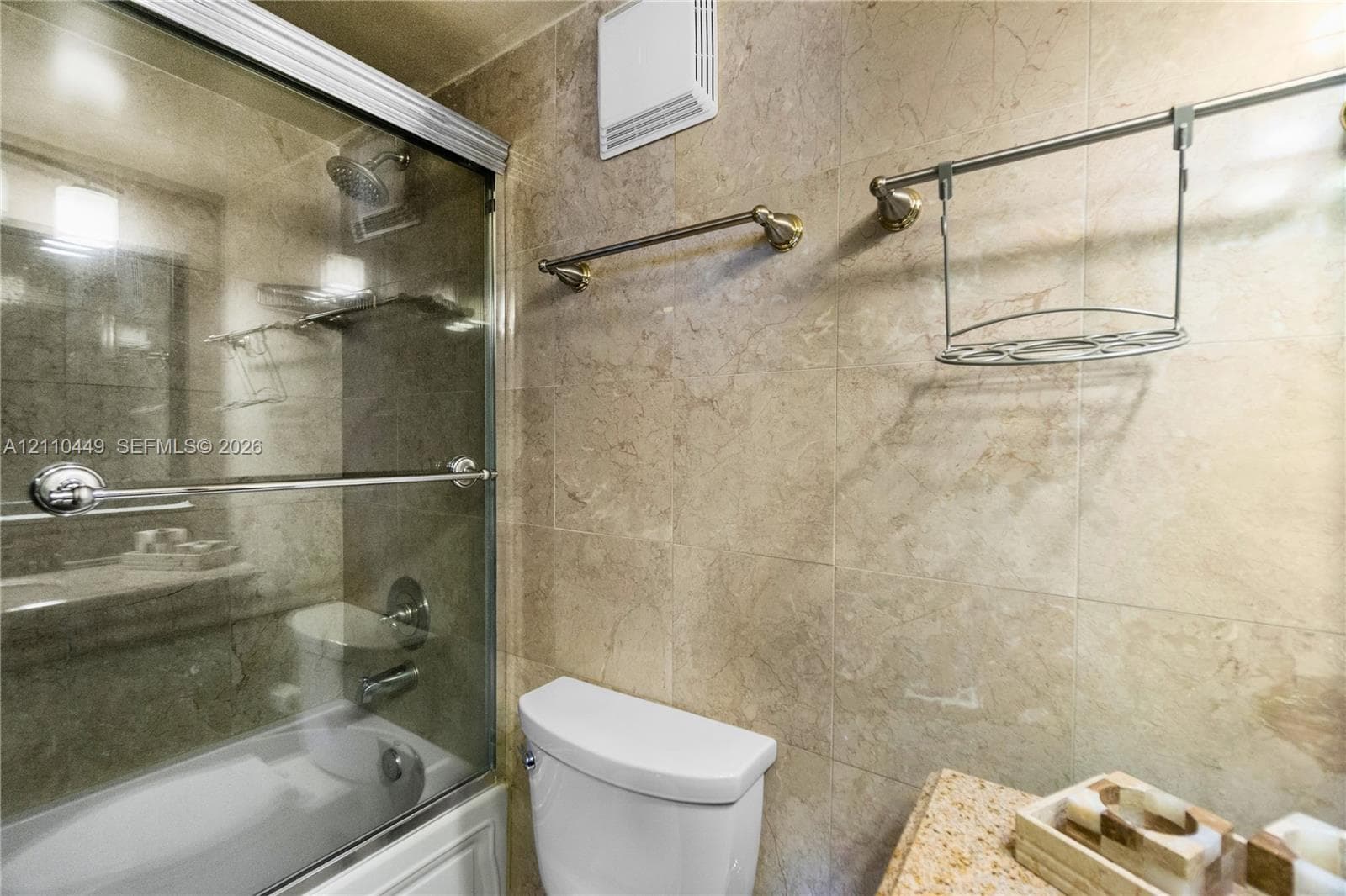 Bathroom featuring floor-to-ceiling stone tile, a glass-enclosed shower, brushed nickel fixtures, and wall-mounted metal shelving