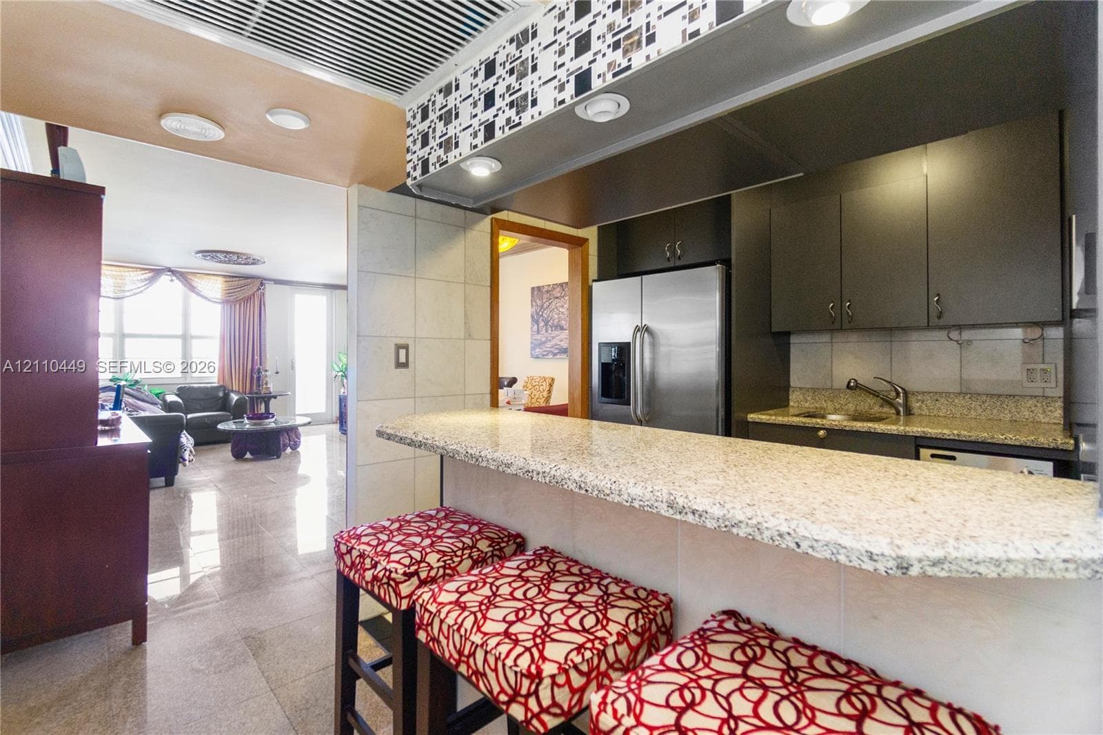 Kitchen featuring a stone-surfaced breakfast bar, flat-panel cabinetry, built-in stainless steel refrigerator, recessed lighting, and polished flooring