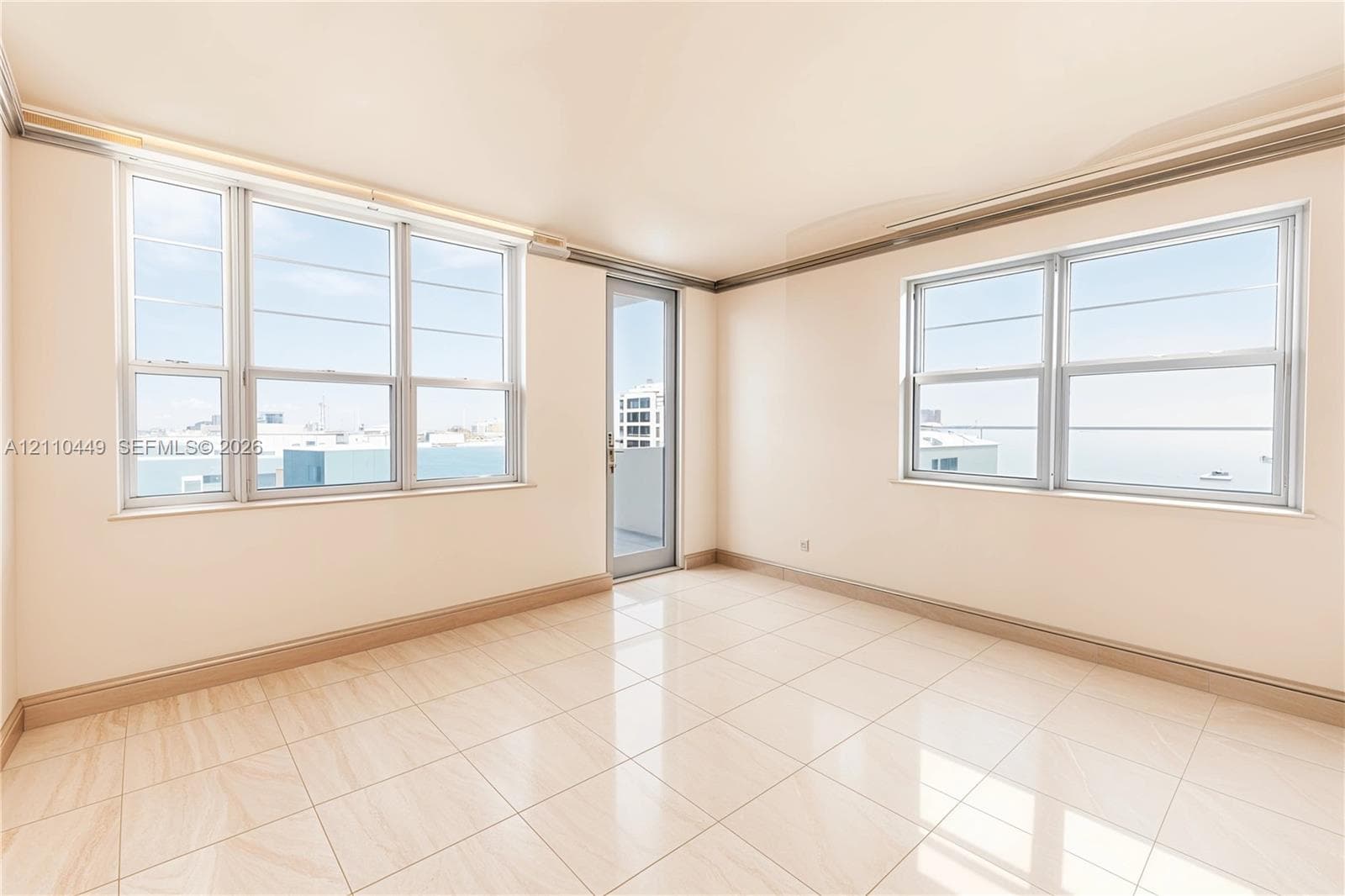 Bright room featuring large multi-pane windows, neutral tile flooring, and a glass-paned door providing external access