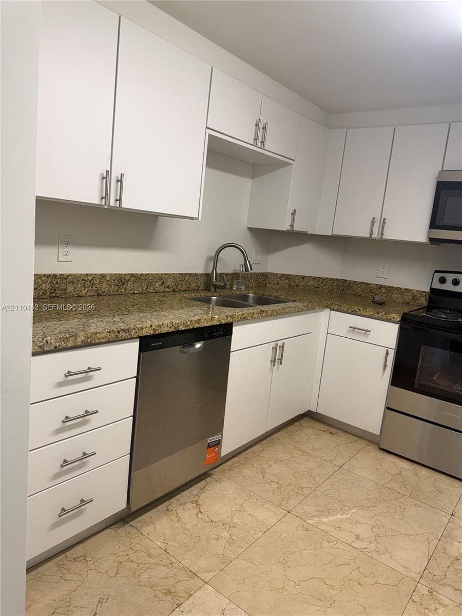 Kitchen featuring white cabinetry with brushed-metal pulls, stone-composite countertops, a stainless steel dishwasher, a double-basin sink with a gooseneck faucet, and stone-tile flooring
