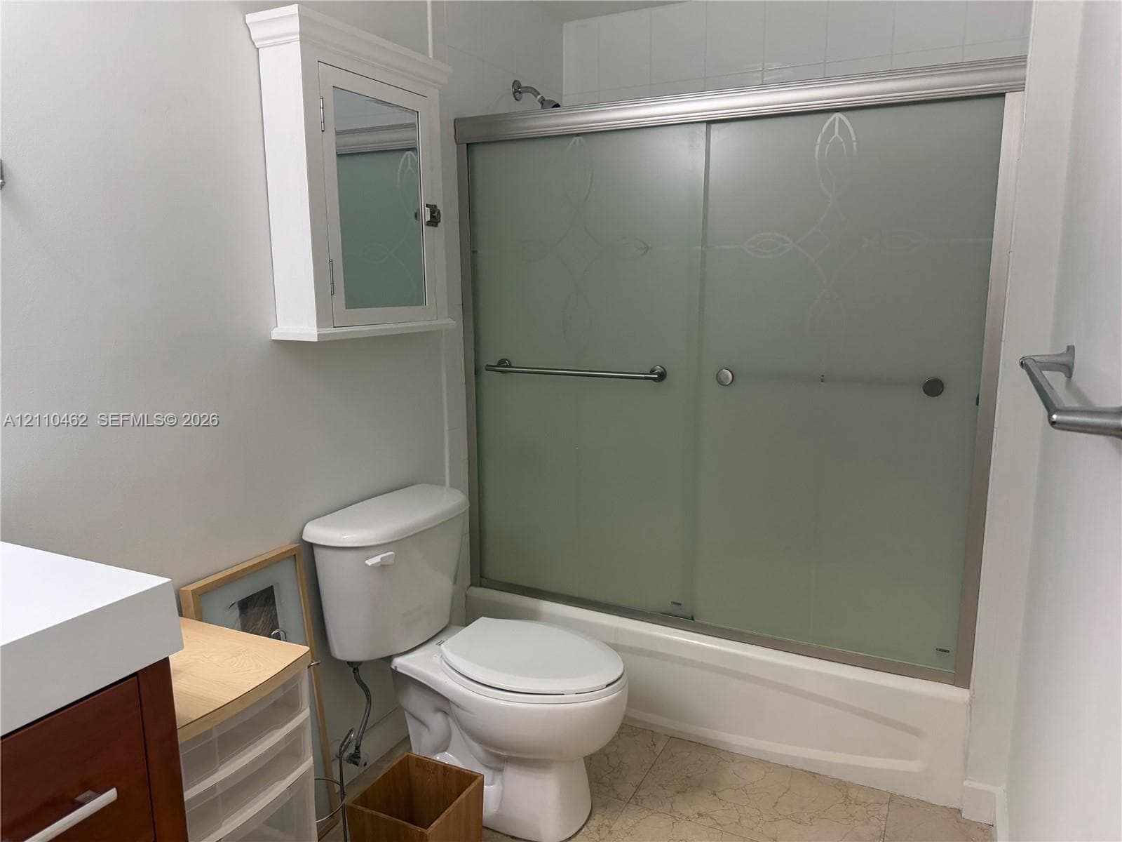 Bathtub with frosted sliding glass doors, wall-mounted medicine cabinet, white toilet, and tile flooring