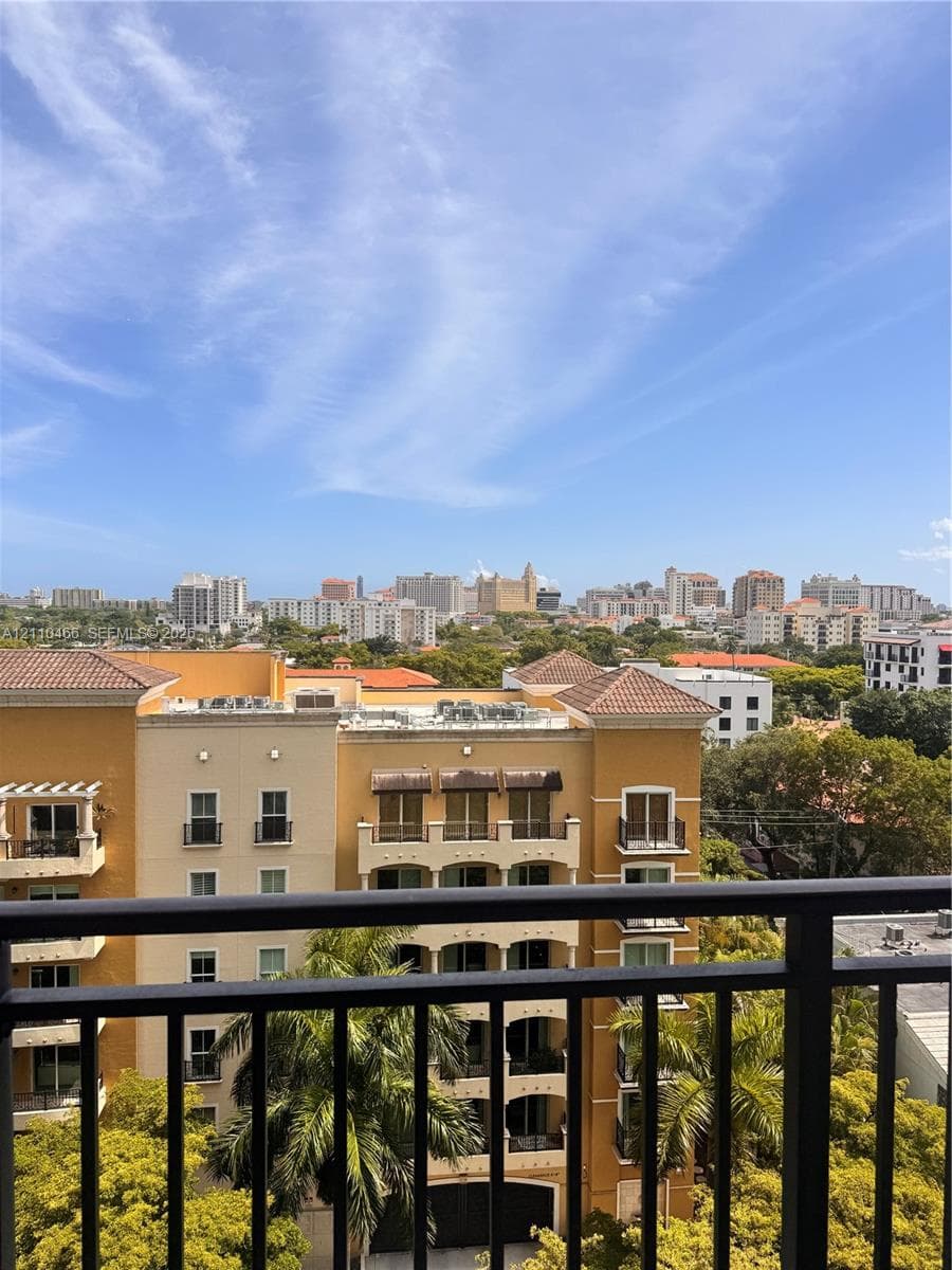 Elevated balcony with a black metal railing overlooking a cityscape and mature canopy trees