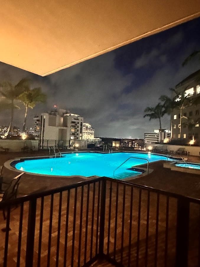 Swimming pool with integrated spa, paved terrace, and metal railings against a city skyline backdrop