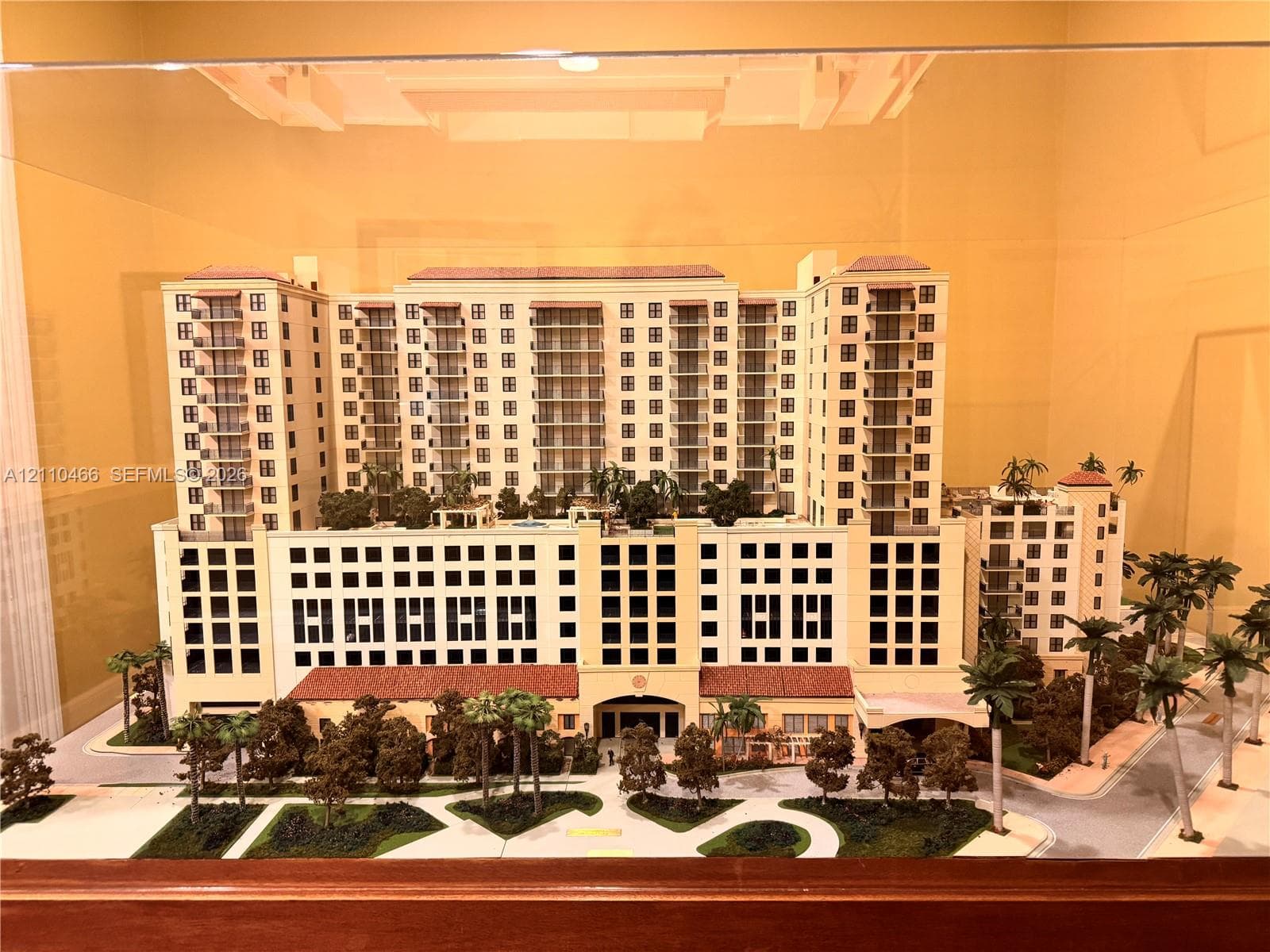 Multi-story architectural scale model featuring a cream-colored facade, terracotta-tiled roof accents, private balconies, and integrated landscaping with mature trees
