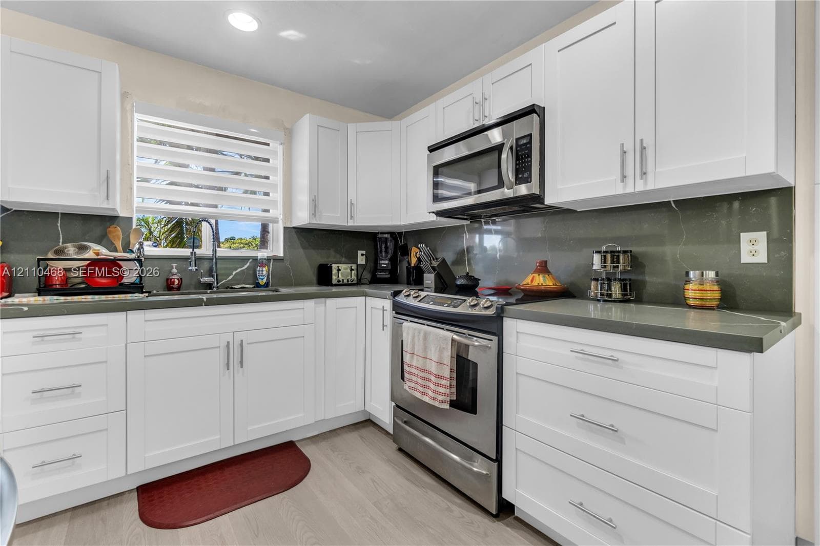 Kitchen featuring white shaker-style cabinetry, solid-surface countertops, full-height backsplash, stainless steel appliances, and wood-finish flooring