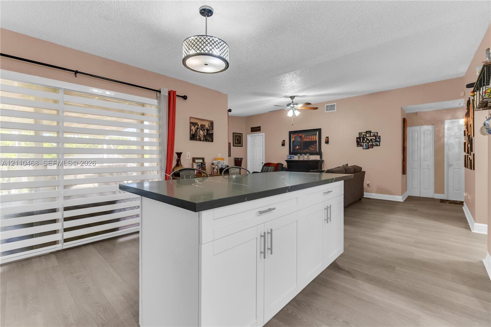 Kitchen island featuring a dark stone-finish countertop and white cabinetry with brushed metal hardware, wood-finish flooring, and a decorative drum pendant light