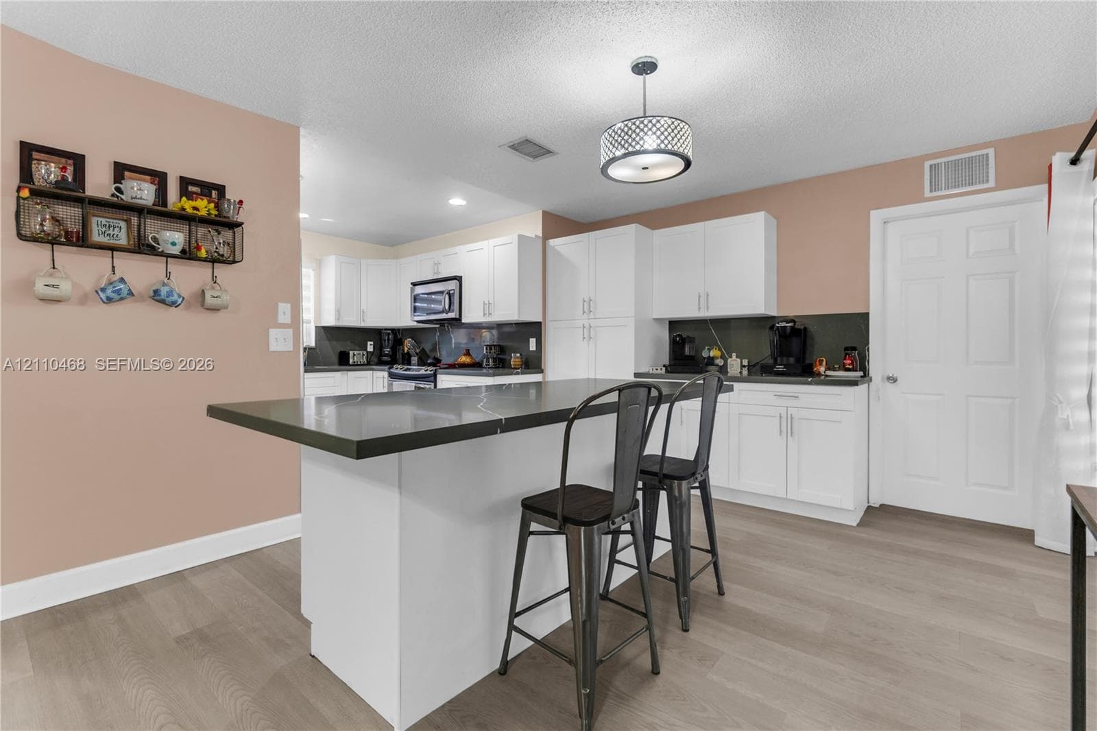 Kitchen featuring white shaker-style cabinetry, a central island with a dark countertop, wood-finish flooring, and a drum-style pendant light fixture