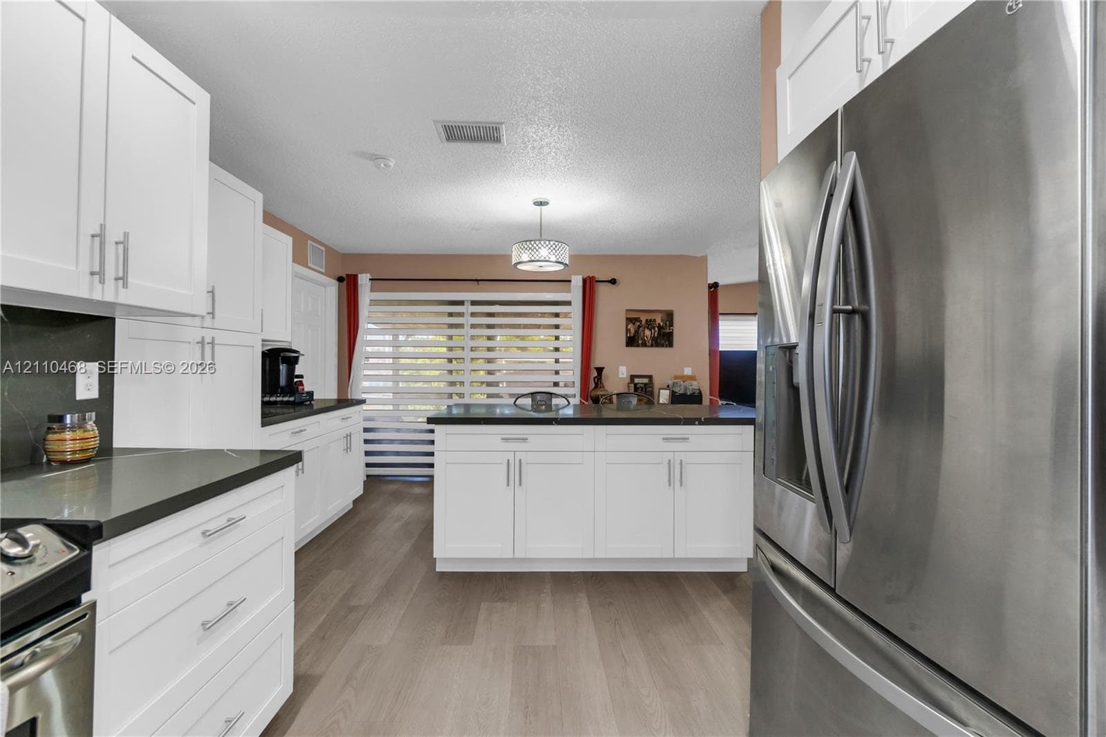 Kitchen featuring white shaker-style cabinetry, dark stone-finish countertops, stainless steel appliances, wood-finish flooring, and a central island