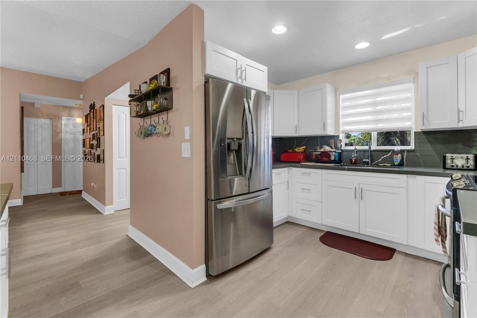 Kitchen featuring white shaker-style cabinetry, stainless steel refrigerator, dark countertops, wood-finish flooring, and recessed ceiling lighting