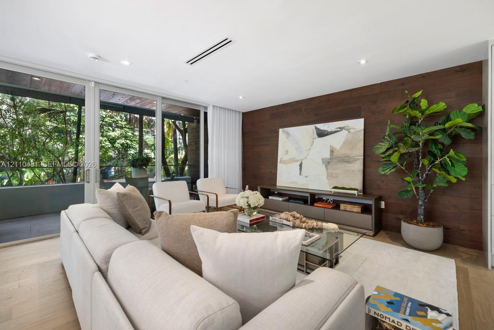 Living area featuring floor-to-ceiling glass sliding doors, rich wood-plank accent wall, recessed lighting, and light-toned wood-finish flooring