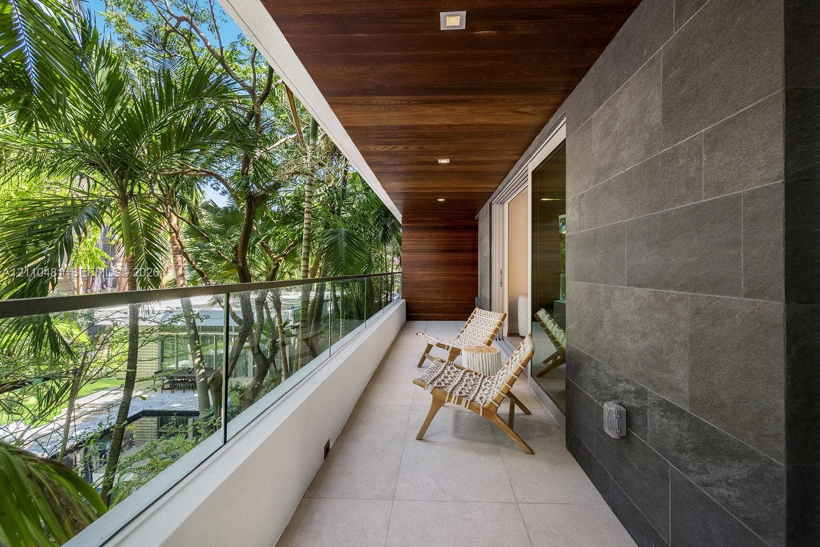 Covered balcony featuring wood-plank ceiling, recessed lighting, large-format tile flooring, a glass panel railing, and charcoal-toned stone wall cladding