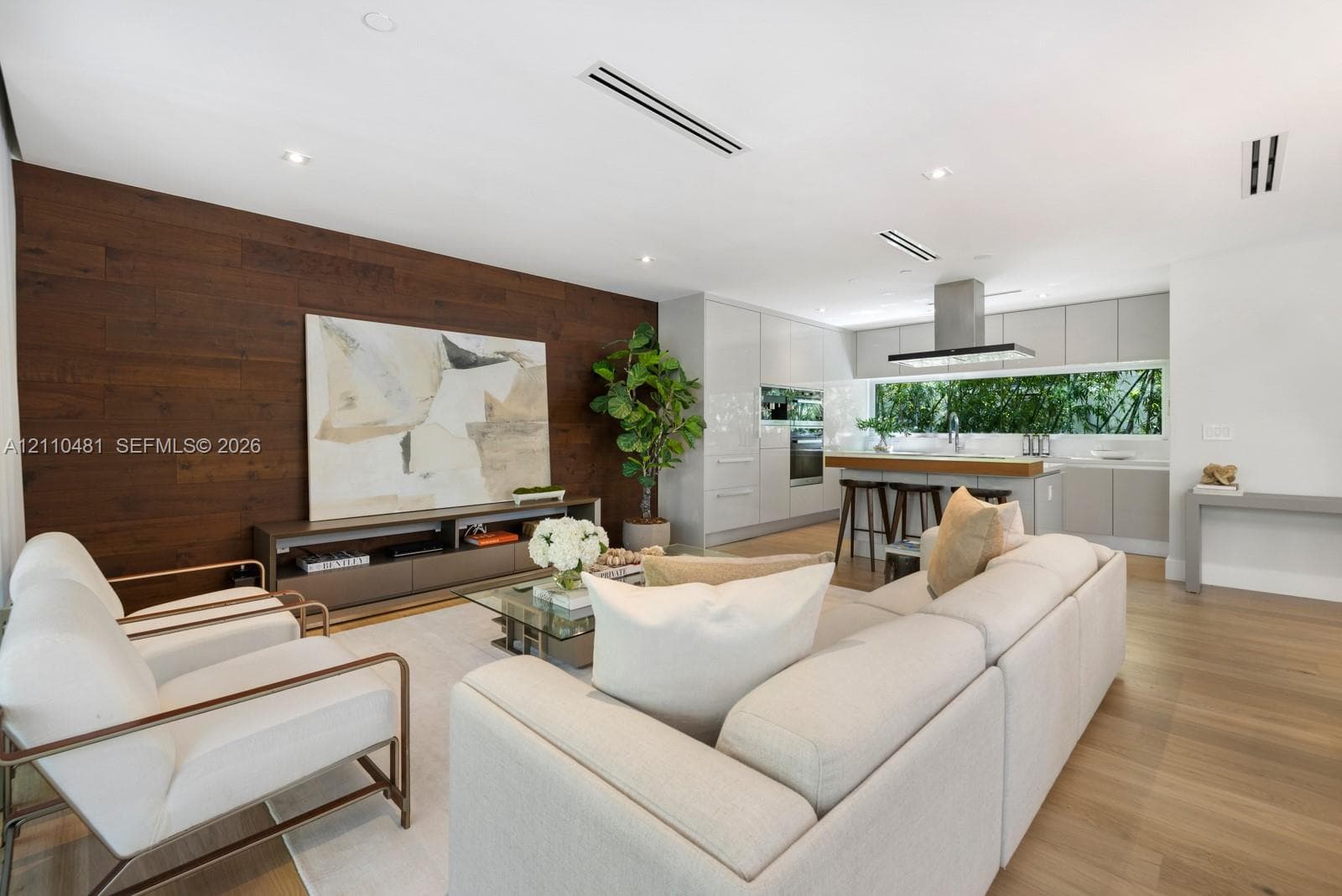 Open-concept space featuring wood-finish flooring, a wood-paneled accent wall, flat-panel cabinetry, a stainless steel range hood, and recessed lighting