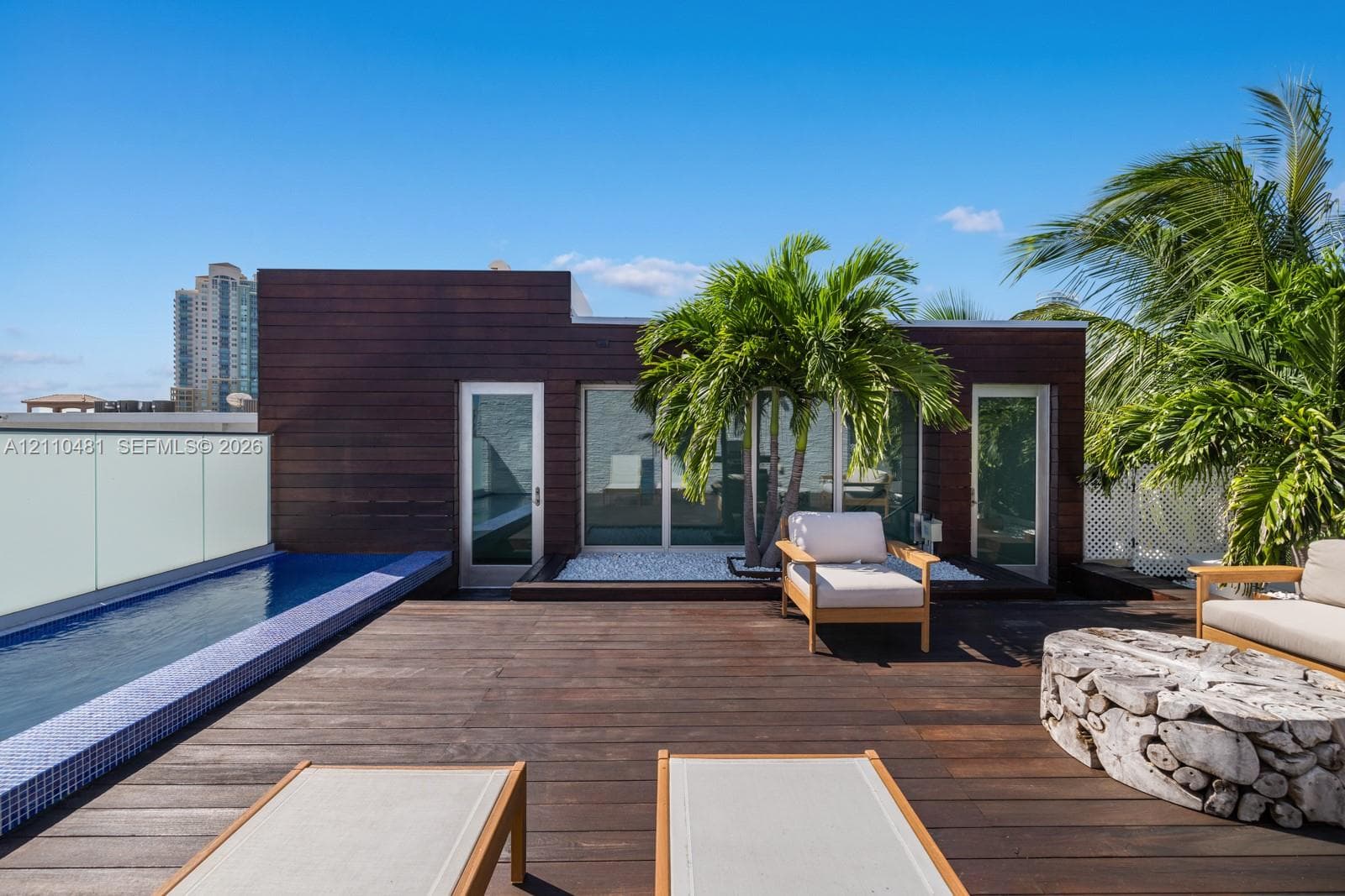 Rooftop terrace featuring dark wood decking, a built-in lap pool with mosaic tile surround, opaque glass railing, and wood-paneled exterior siding