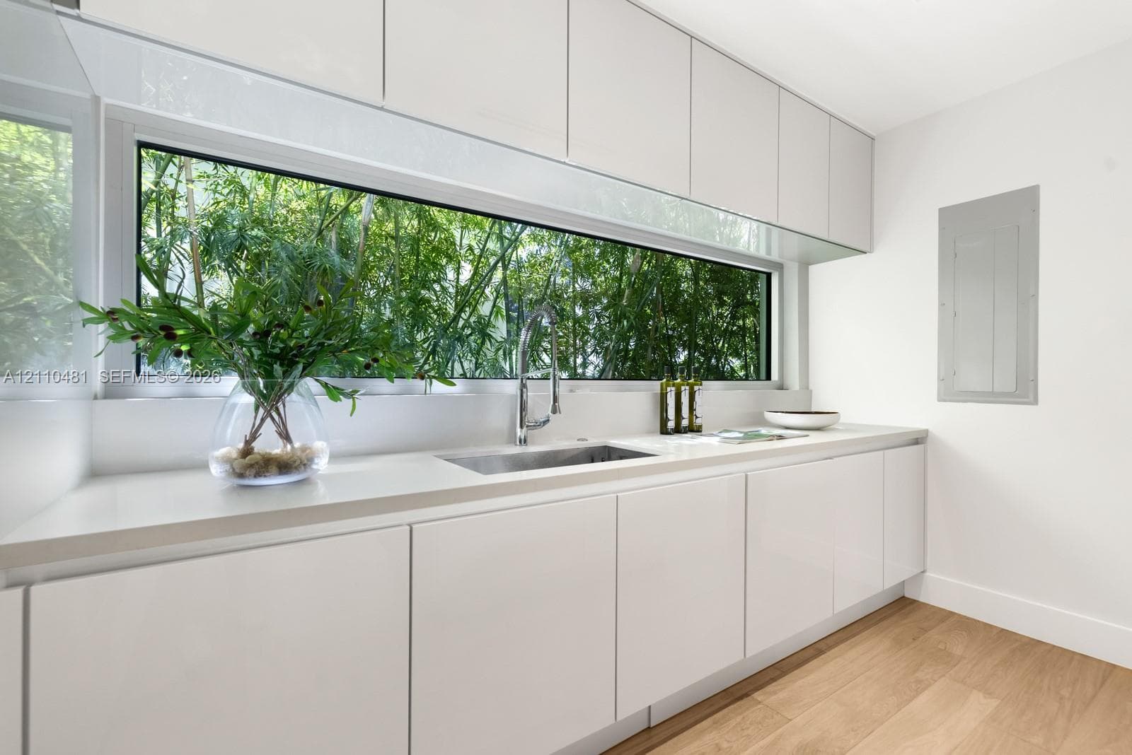 High-gloss white cabinetry, expansive horizontal picture window, solid-surface countertop, stainless steel pull-down faucet, and wood-finish flooring