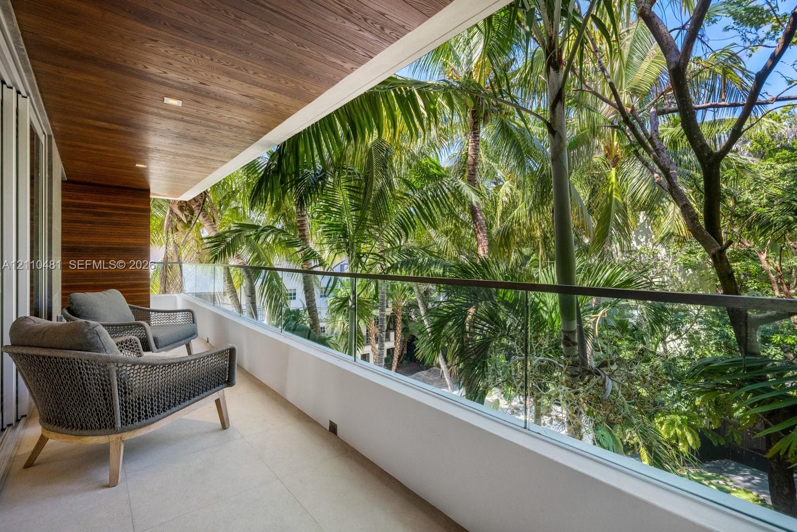 Covered balcony featuring wood-plank ceiling paneling, frameless glass railing, and light-toned tile flooring