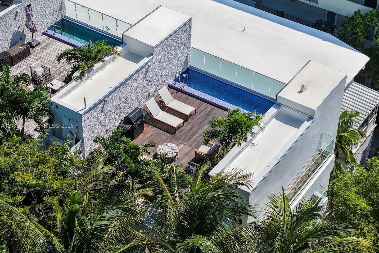 Rooftop terrace featuring wood decking, tiled pool, glass railing, and textured exterior wall cladding