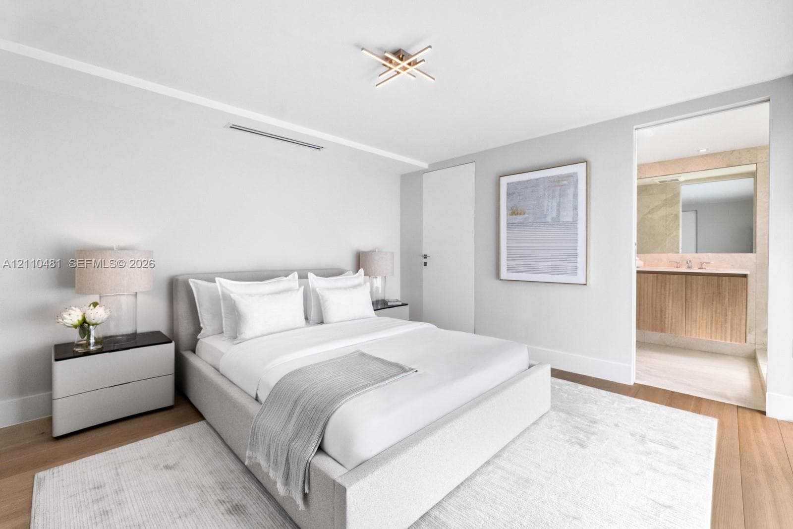 Modern bedroom featuring wide-plank wood-finish flooring, a linear ceiling light fixture, and an ensuite bathroom with a floating vanity and natural stone wall accents