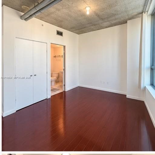 Exposed concrete ceiling, dark wood-finish flooring, floor-to-ceiling windows, and double-door closet