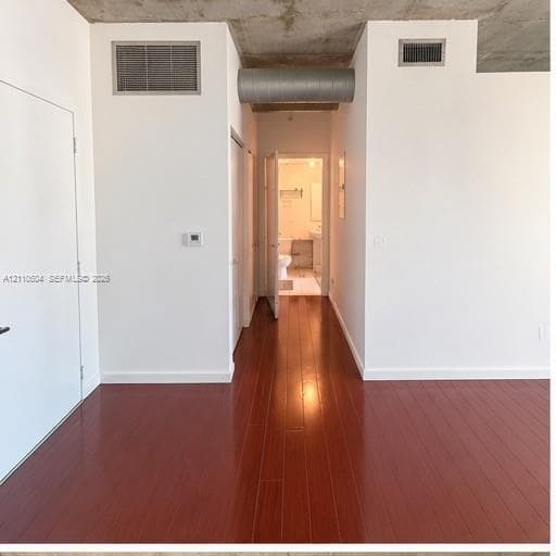 Exposed concrete ceiling with industrial ductwork, polished wood-finish flooring, and crisp white wall finishes