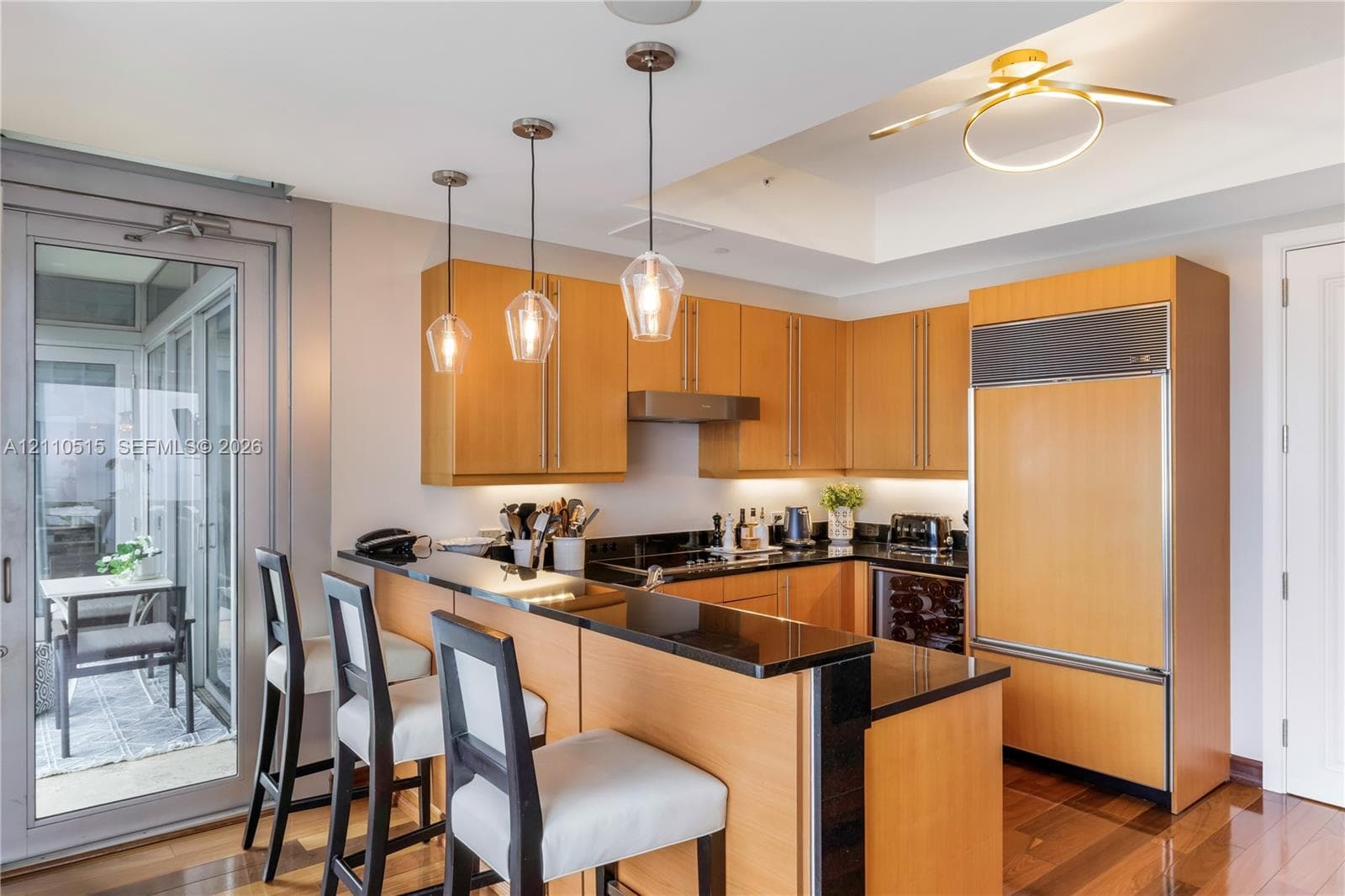Kitchen featuring custom light-finish cabinetry, dark solid-surface countertops, built-in panel-ready refrigerator, under-cabinet lighting, and suspended glass pendant fixtures