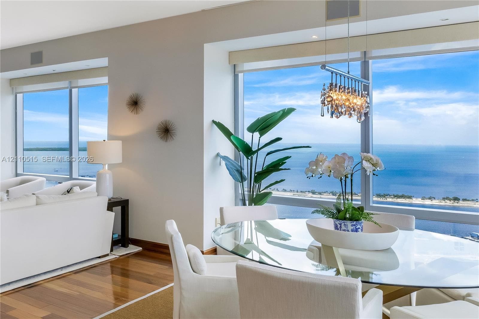 Floor-to-ceiling windows, wood-finish flooring, and a multi-tiered crystal chandelier