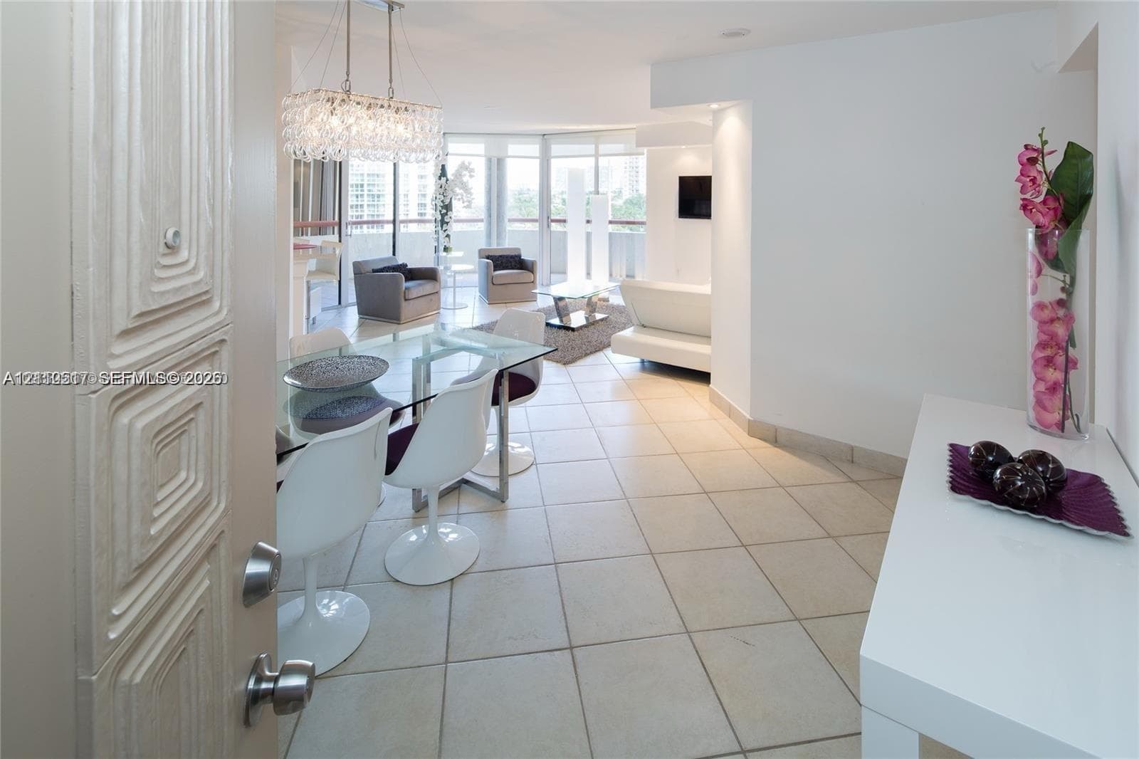 Large-format tile flooring, crystal-accented chandelier, and floor-to-ceiling glass paneling featuring balcony access