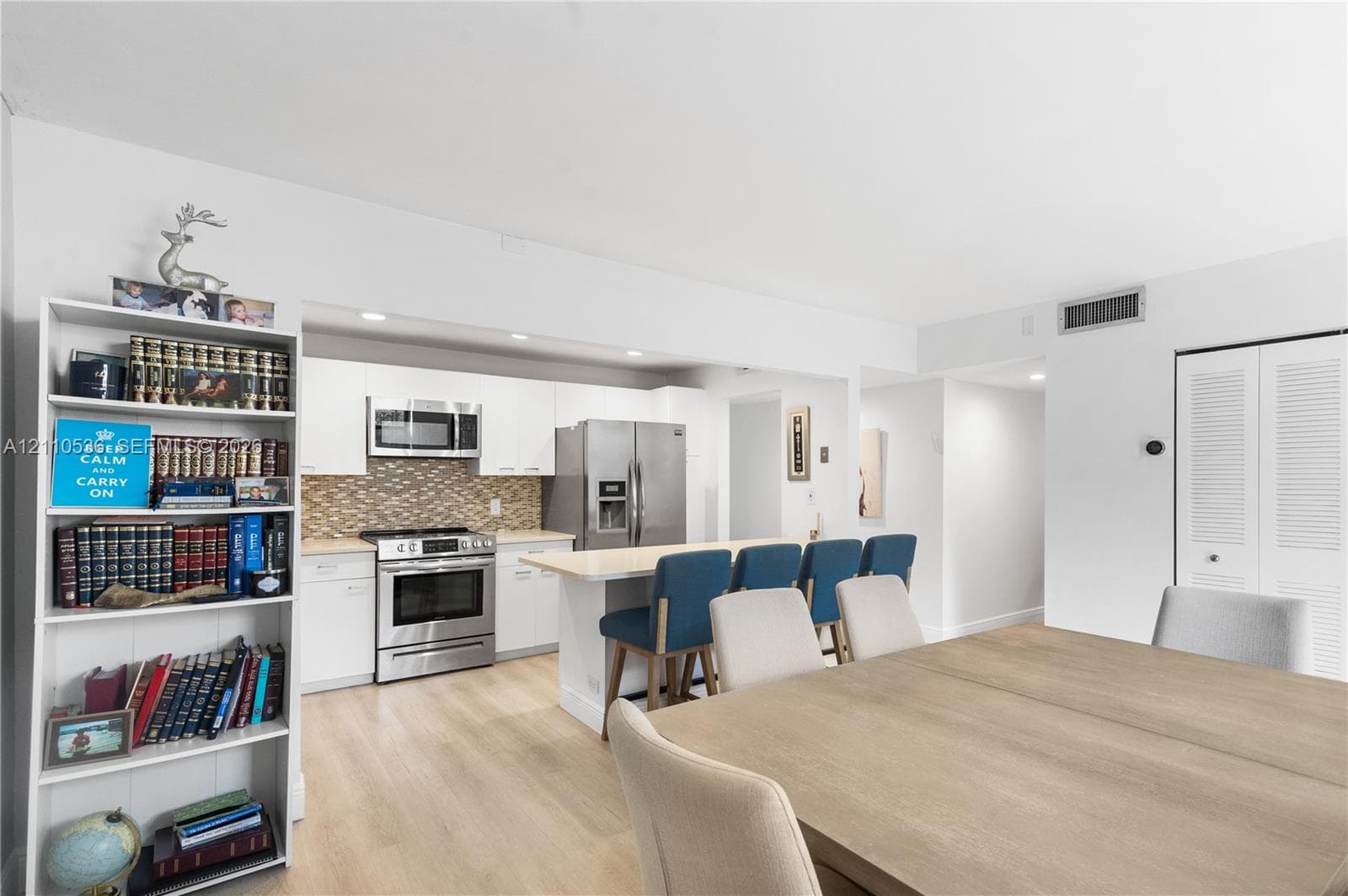 Kitchen featuring white cabinetry, stainless steel appliances, a center island with counter seating, and a decorative tile backsplash, complemented by wood-finish flooring