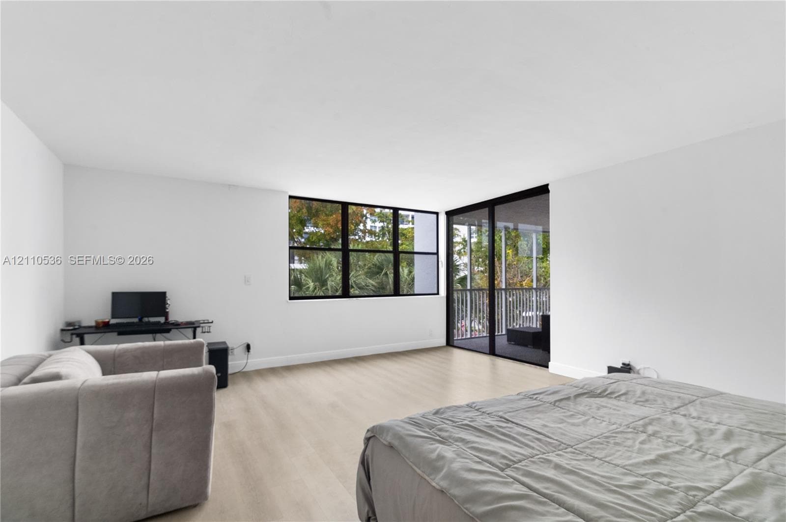 Interior space featuring wood-finish flooring, white walls, multi-pane black-framed windows, and a sliding glass door opening to a railed balcony