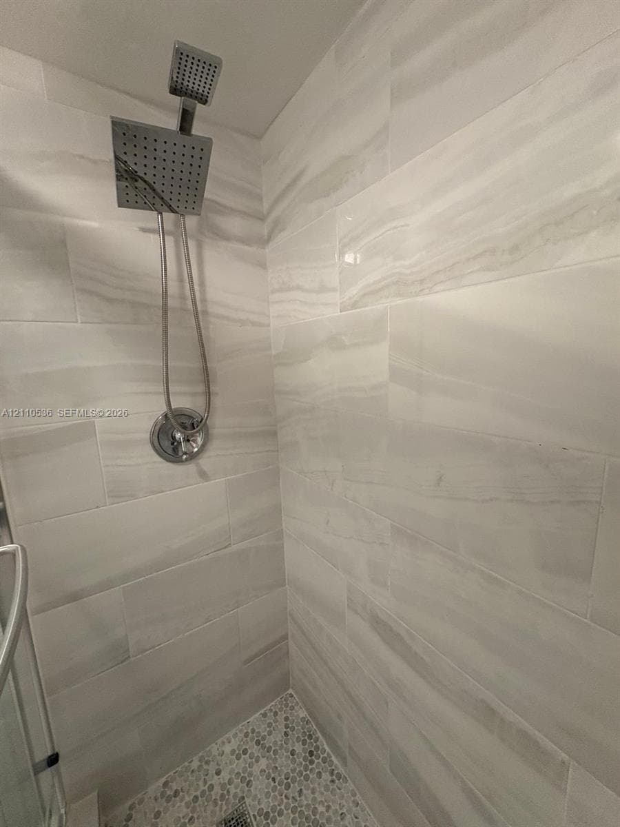 Shower stall featuring large-format stone-patterned wall tile, pebble-texture floor tile, and a polished chrome square rainfall showerhead with a handheld sprayer