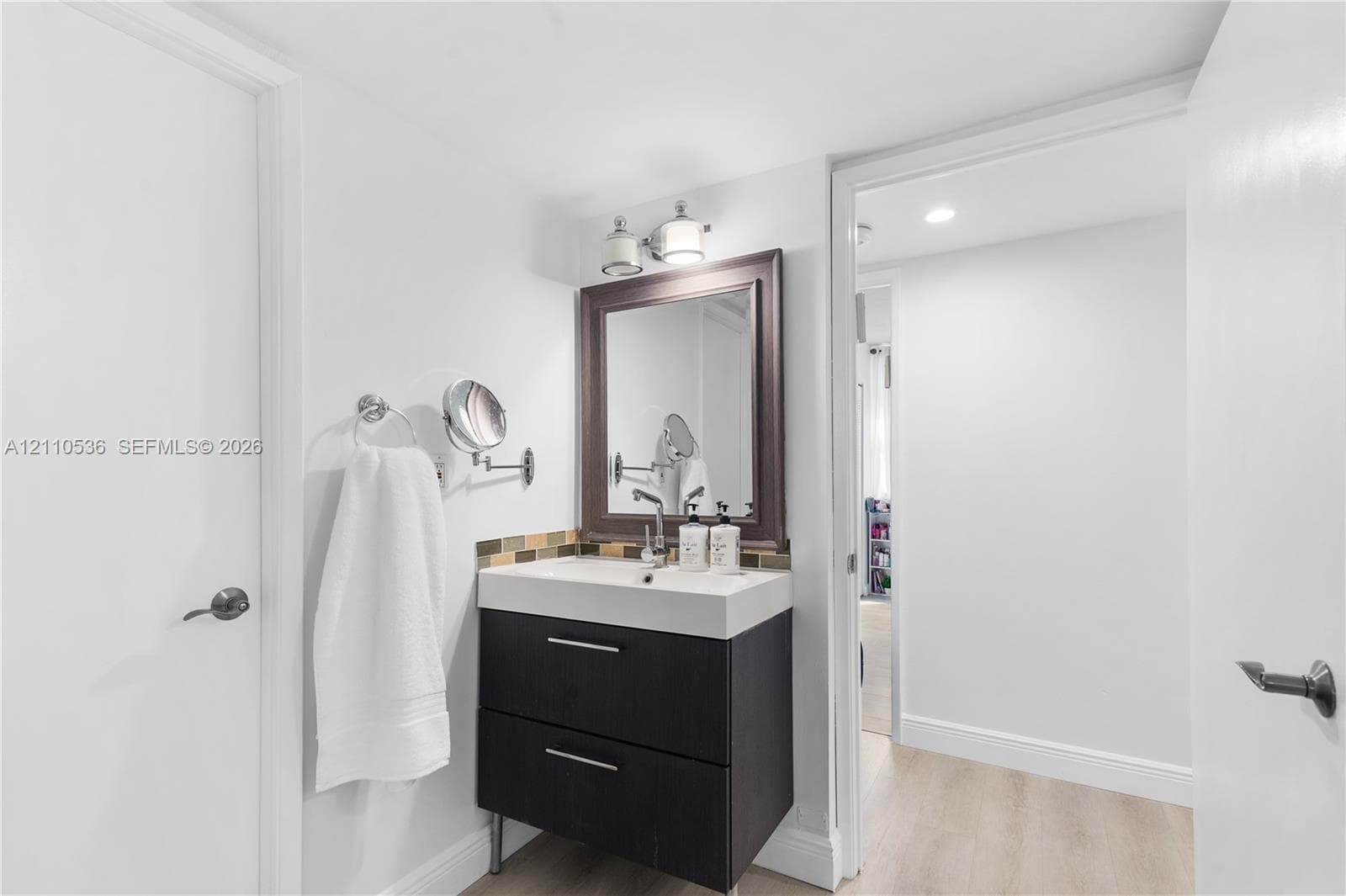 Dark wood-finish vanity with two drawers, integrated white basin, framed wall mirror, multi-toned tile backsplash, and dual-light fixture