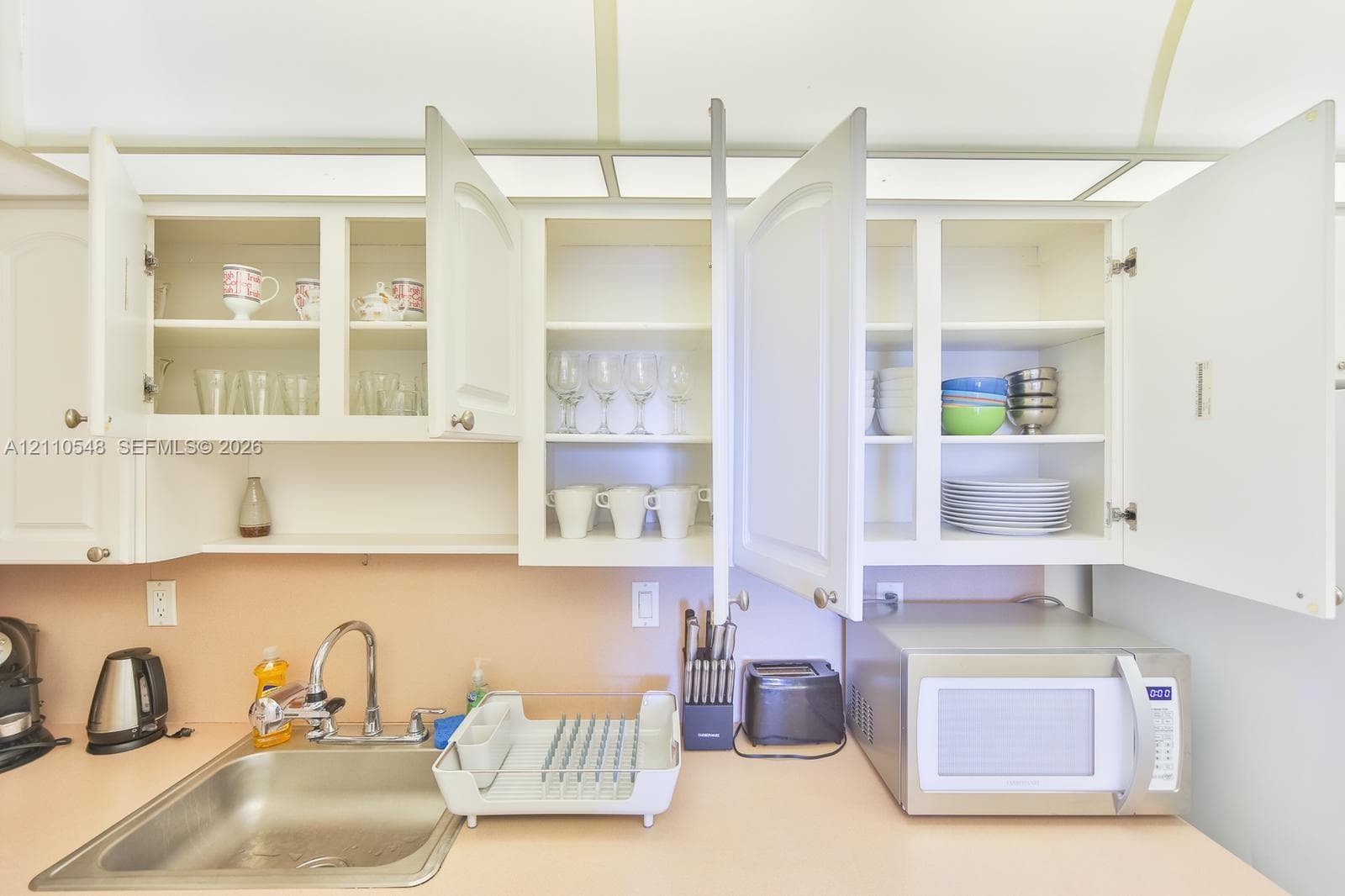 White cabinetry with paneled doors, solid-surface countertop, stainless steel sink, and integrated overhead lighting