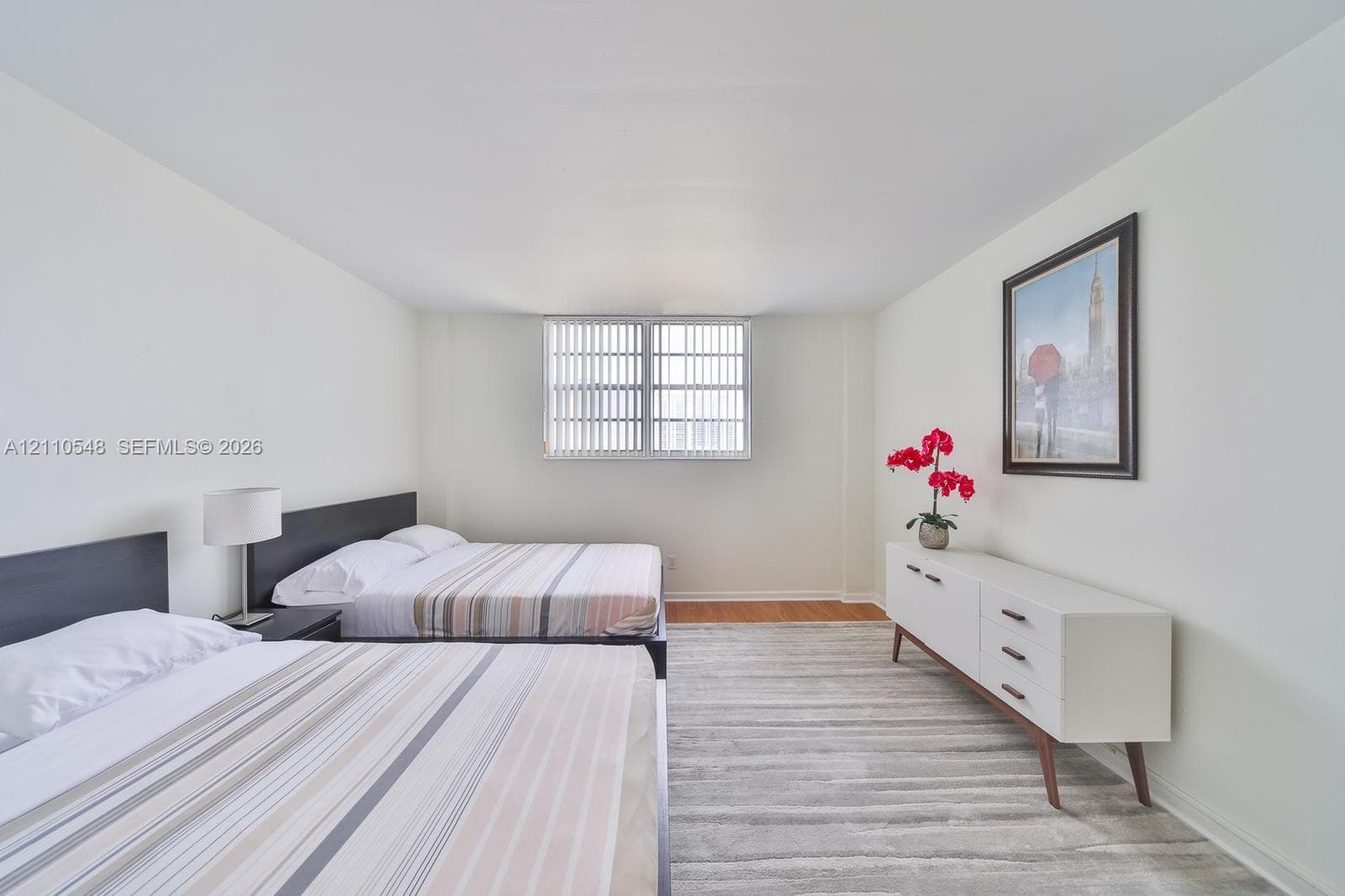 Spacious room featuring neutral paint, wood-finish flooring, and a large window with vertical blinds