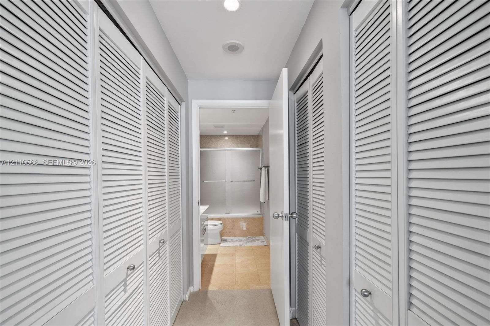 Hallway featuring white louvered-style closet doors, recessed ceiling lighting, and tile flooring