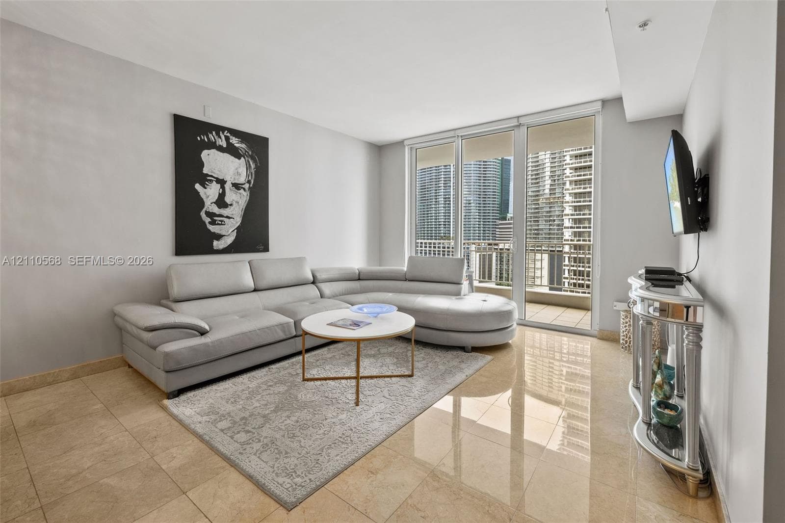 Living area featuring neutral-toned tile flooring, floor-to-ceiling glass panel doors, and an attached balcony