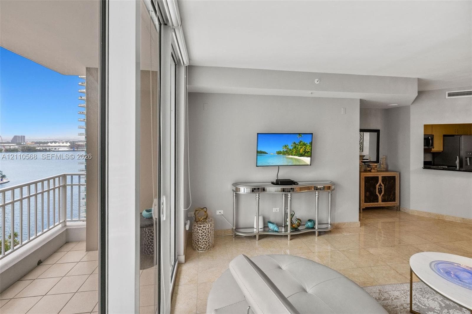 Living area featuring polished stone tile flooring, floor-to-ceiling sliding glass doors, and a tiled private balcony with metal railing overlooking the water