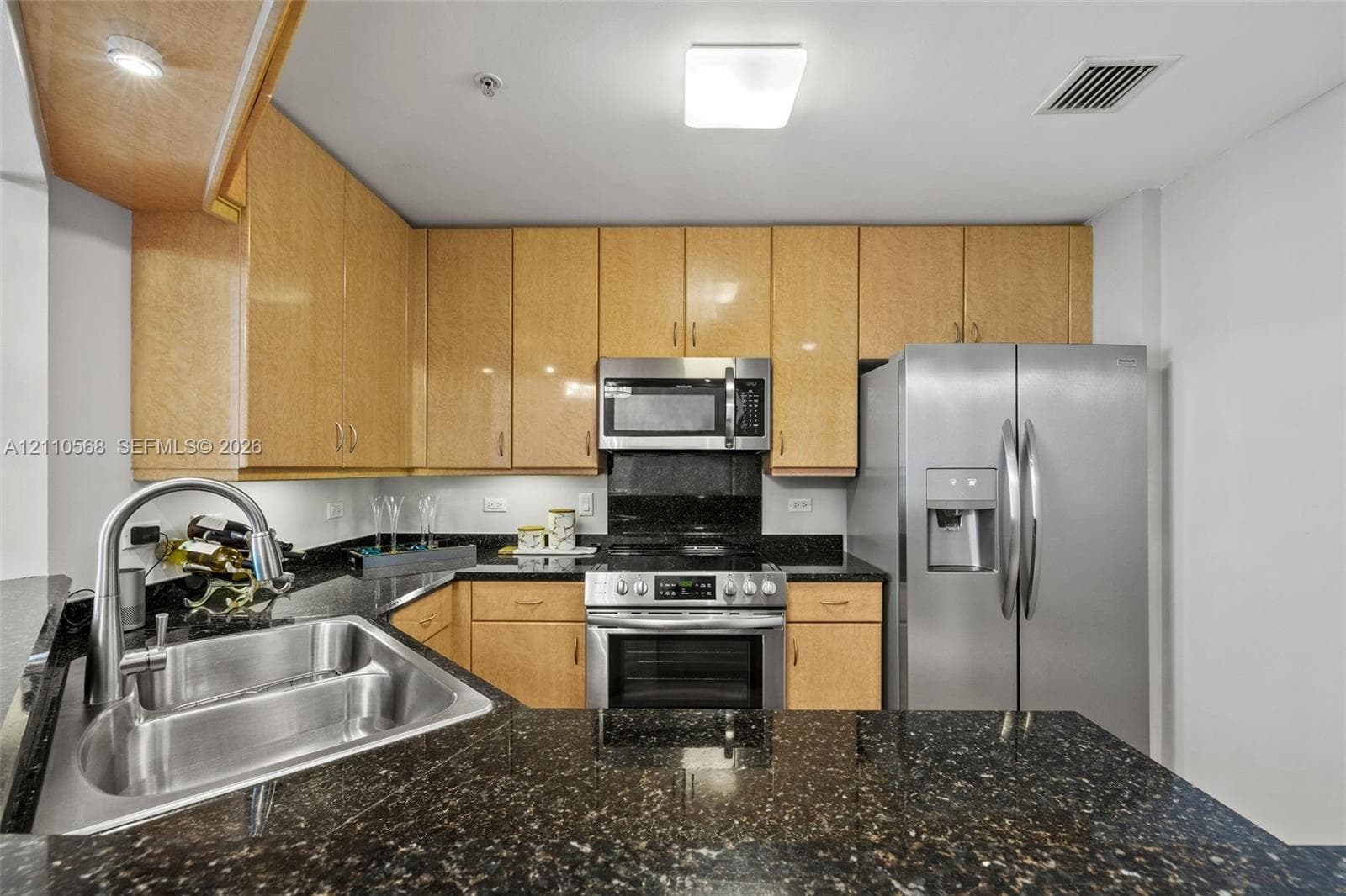 Kitchen featuring light-finish wood cabinetry, dark stone countertops, stainless steel appliances, and a double-basin undermount sink with a gooseneck faucet