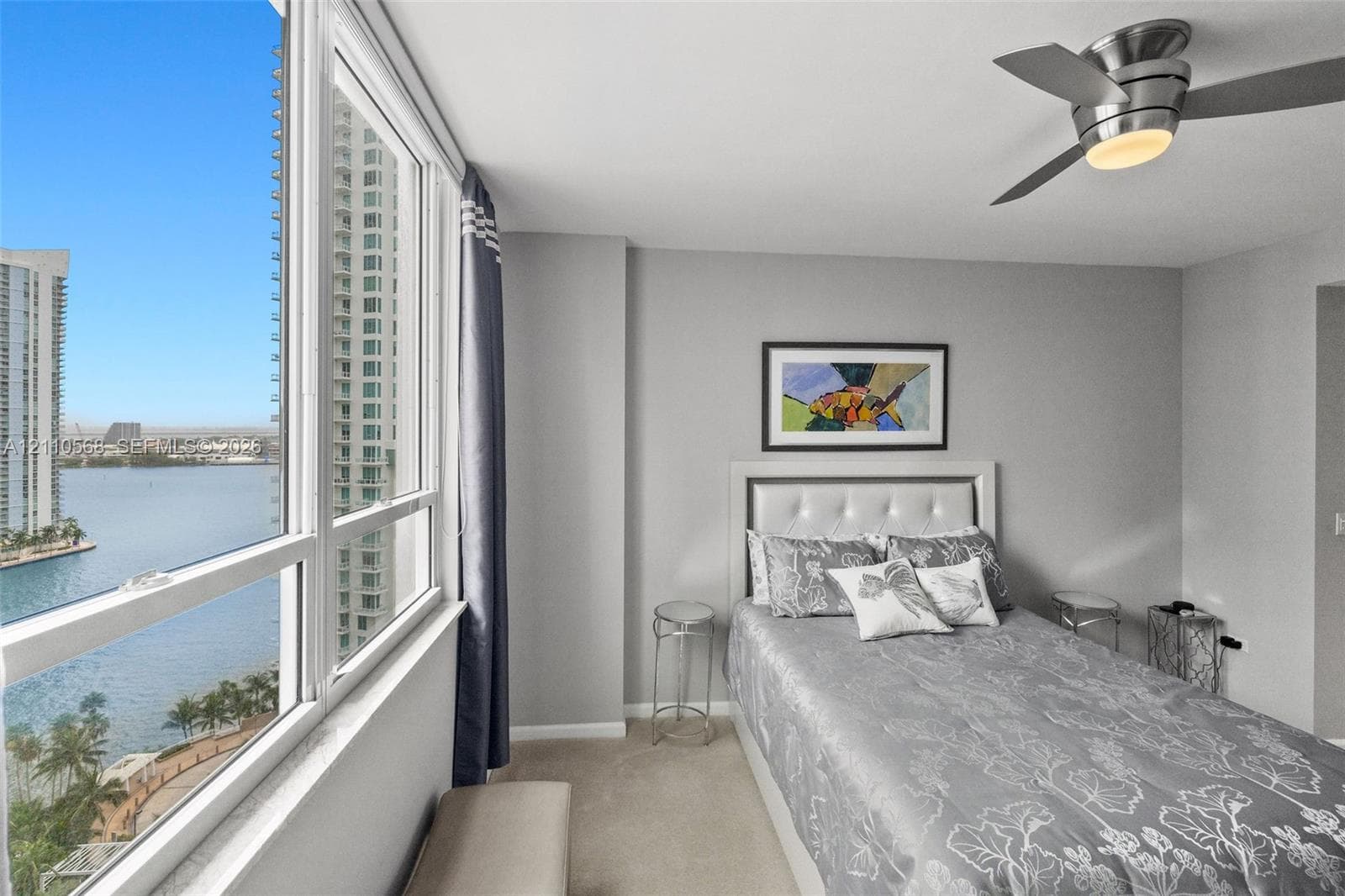 Floor-to-ceiling windows, water-facing exposure, neutral wall palette, and ceiling-mounted light fixture with fan