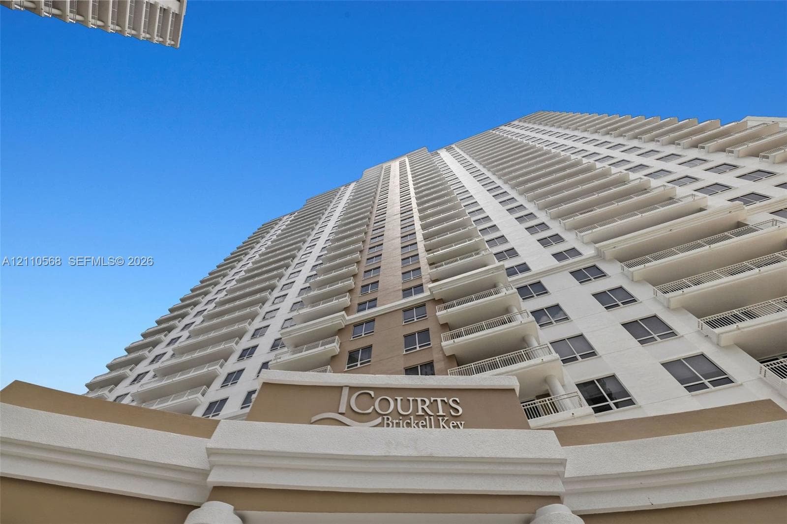 High-rise exterior architecture featuring stacked private balconies, a multi-story neutral facade, and column-supported entryway signage