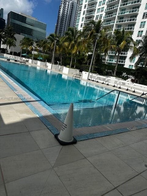 Rectangular swimming pool with light-colored tile decking, perimeter landscaping, and integrated metal handrails