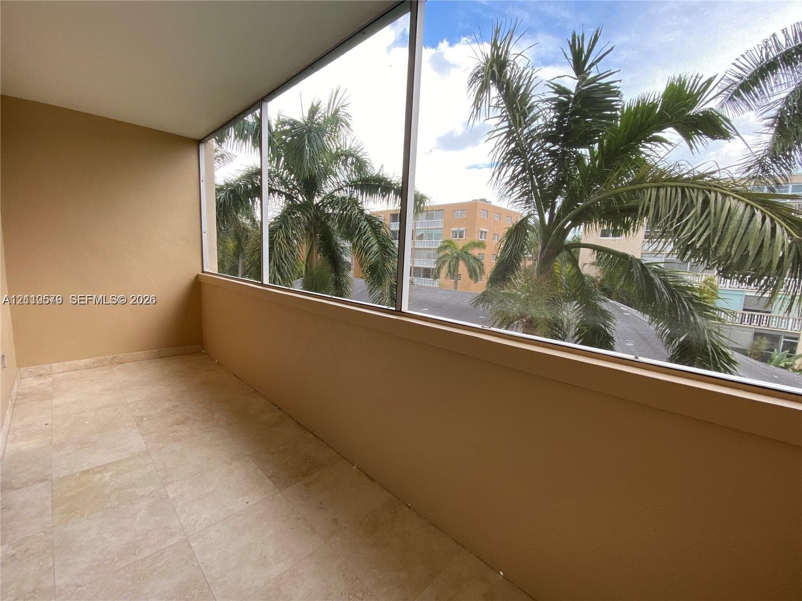 Enclosed balcony featuring light-toned tile flooring, solid wall construction, and expansive screened window panels