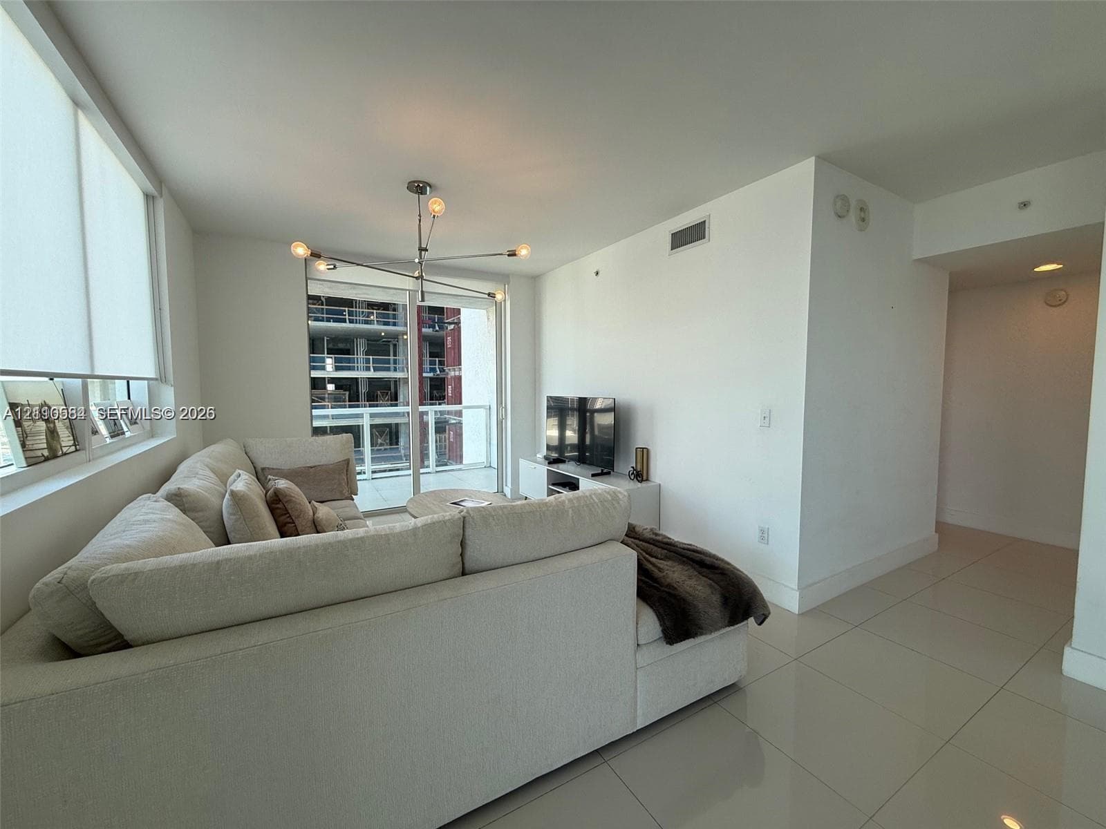 Living area featuring floor-to-ceiling windows, polished tile flooring, a multi-arm modern pendant light, and sliding glass doors with access to a private balcony