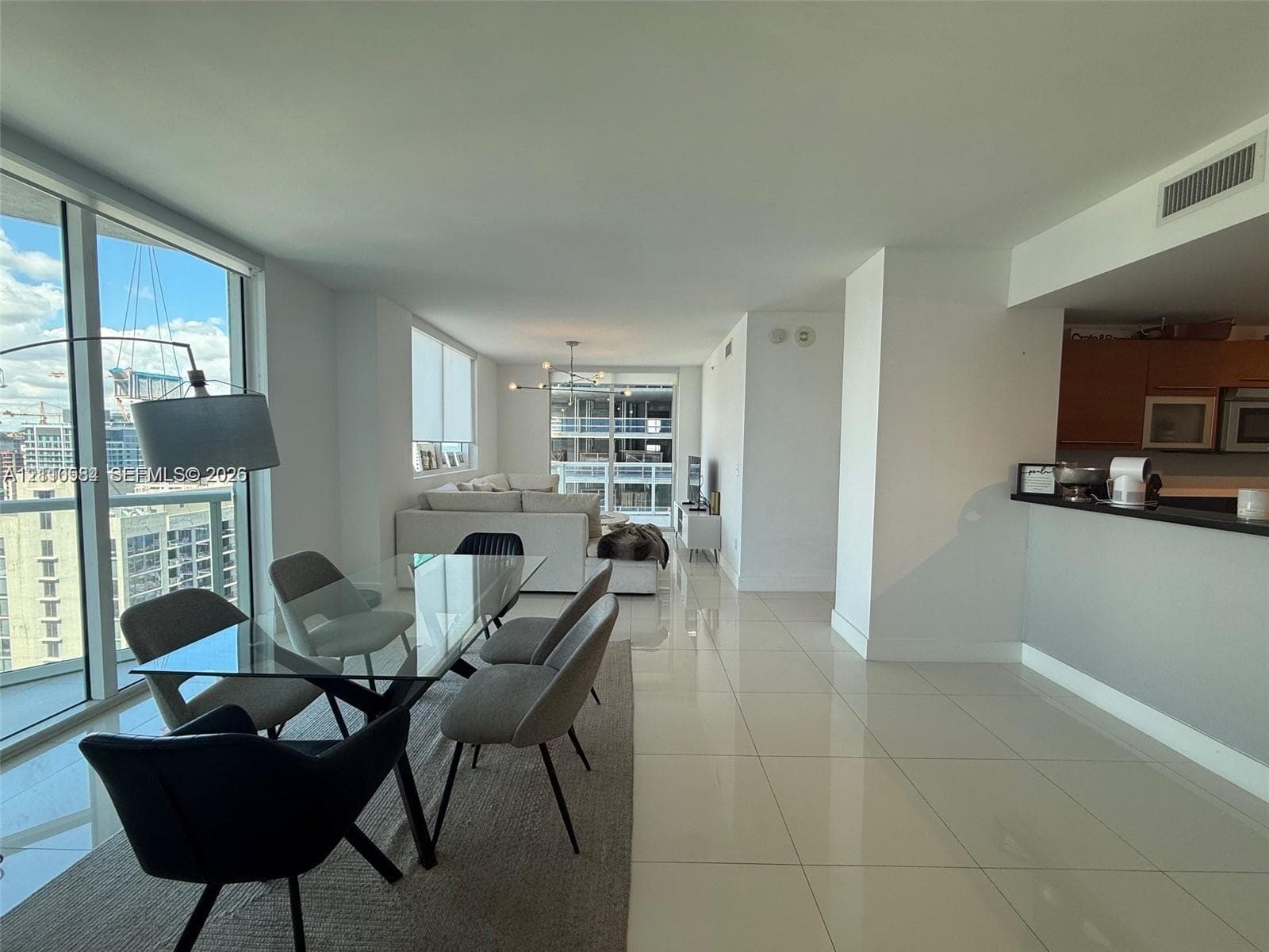 Open-concept interior featuring floor-to-ceiling glass windows, polished tile flooring, and a kitchen peninsula with a dark stone countertop
